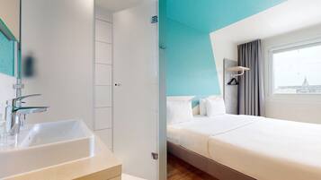 A hotel room with a large bed, a bathroom with a sink, and a view of a cityscape through the window.