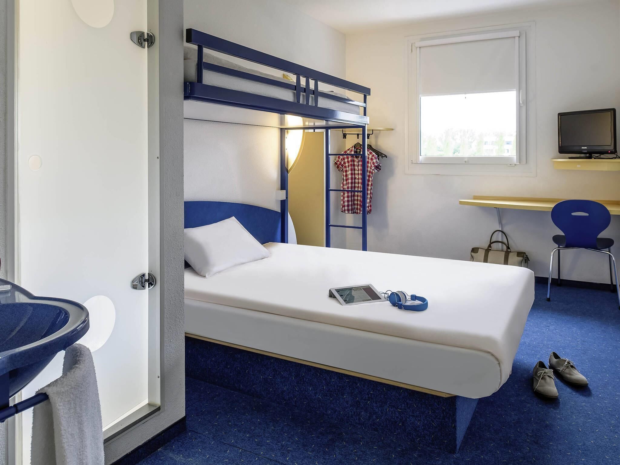Une chambre d’hôtel avec un lit superposé, un bureau, une chaise, une télévision et une fenêtre.