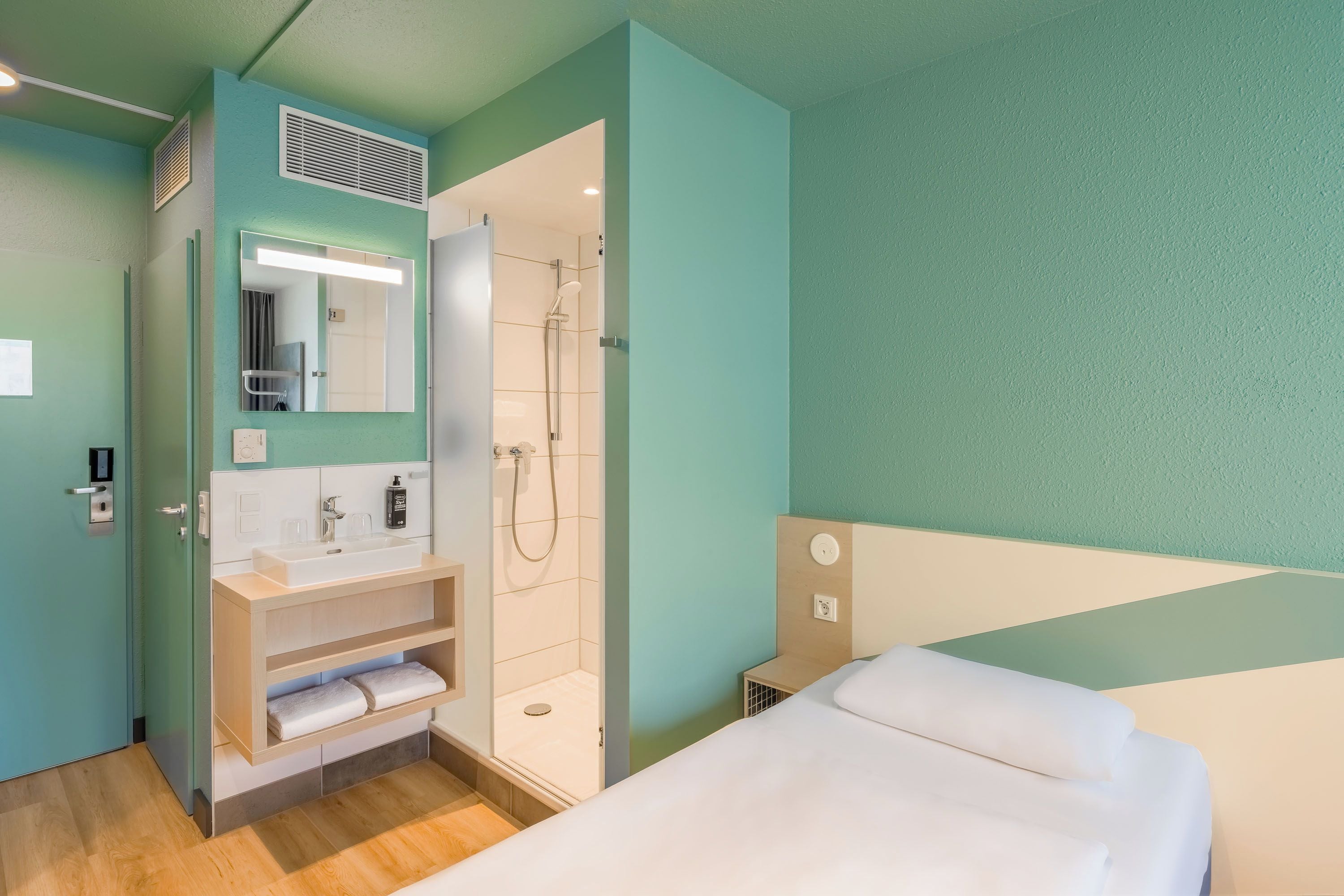 A hotel room with a shower, a sink, a mirror, and a bed.