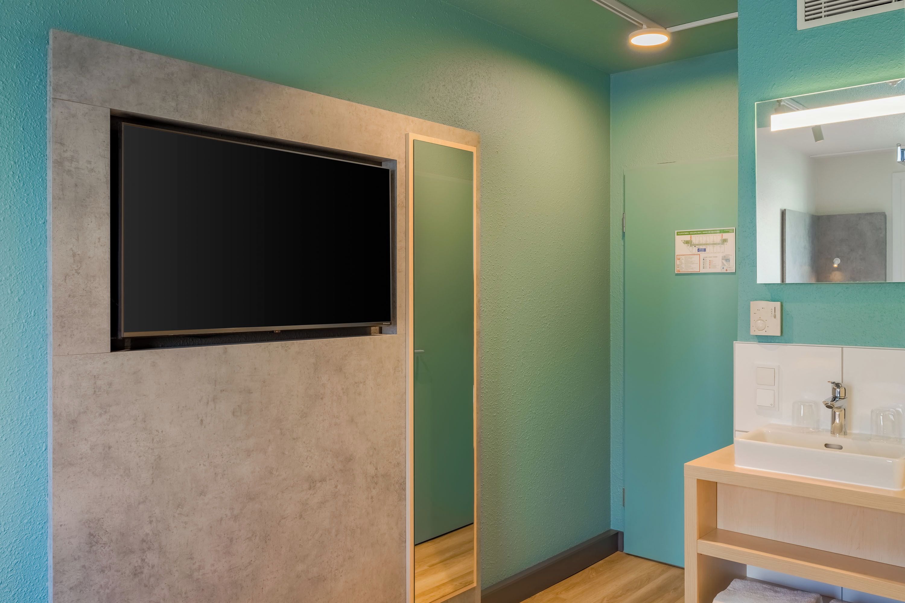 A bathroom with a large mirror, a sink, and a flat-screen TV mounted on the wall.