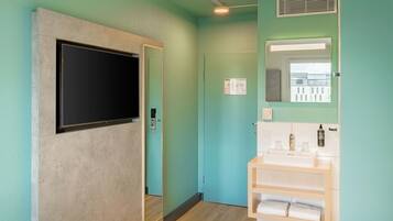 A bathroom with a TV mounted on the wall, a sink with a mirror above it, and a door leading to another room.