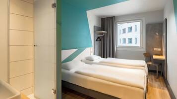 A hotel room with a bed, a desk, and a view of a building through a window.