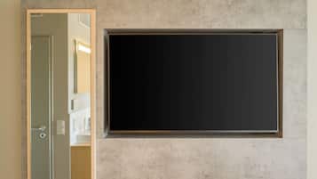 A room with a large, dark-colored flat-screen TV mounted on a textured wall, a door leading to another room, and a small shelf with a few items.