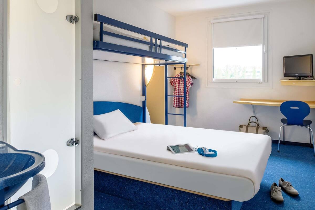 Habitación de hotel con literas, un escritorio con silla, televisor y ventana con vista a edificios.