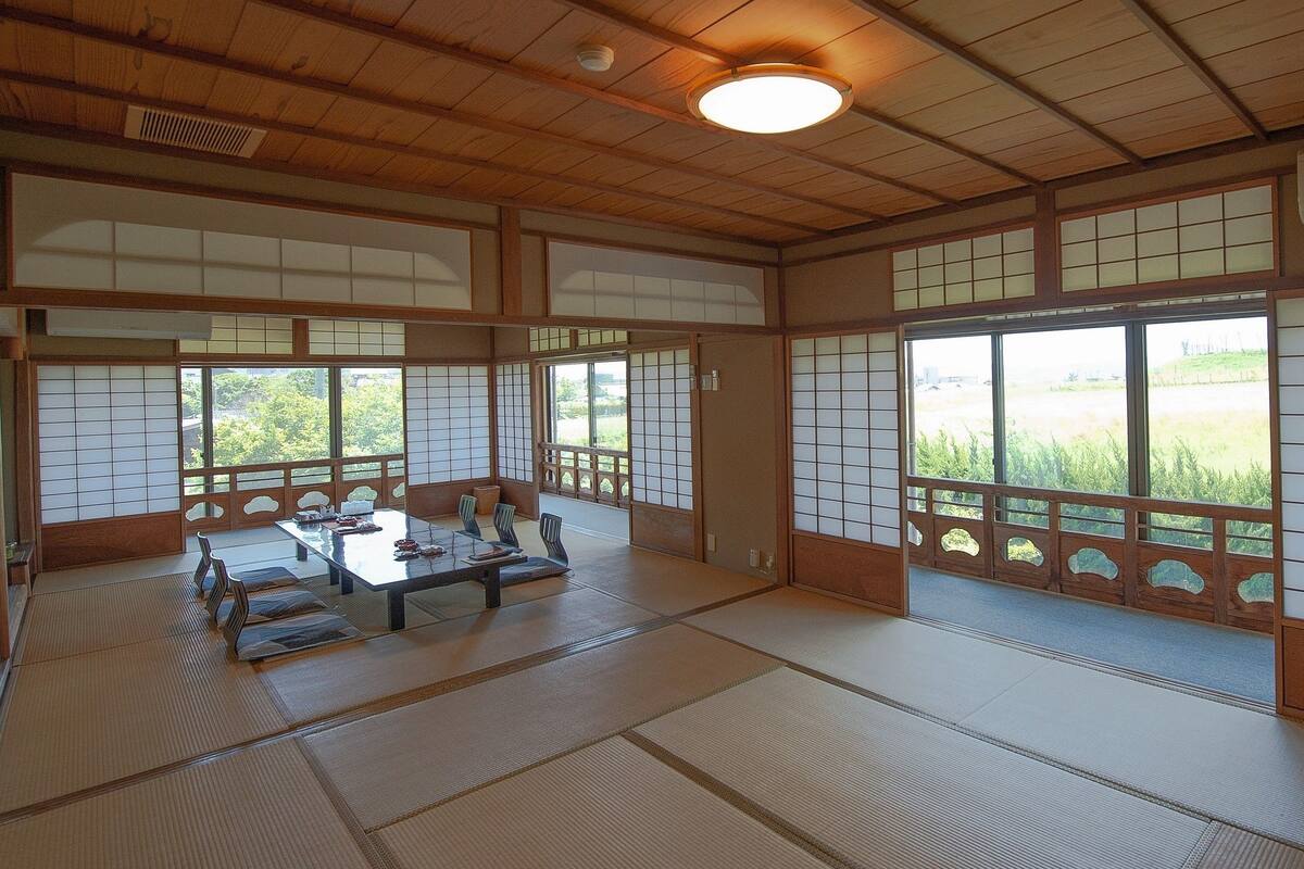 Una habitació tradicional japonesa amb sòls de tatami, una taula baixa amb coixins i grans finestres amb marc de fusta.
