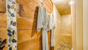 A wooden wall with a stone mosaic, two striped robes hanging, and a shower area with a pebble floor. - Azalea Plantation B&B (Fort Worth)