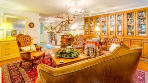 A spacious living room with a large sofa, a wooden cabinet with glass doors, and a staircase leading to an upper floor. - Azalea Plantation B&B (Fort Worth)
