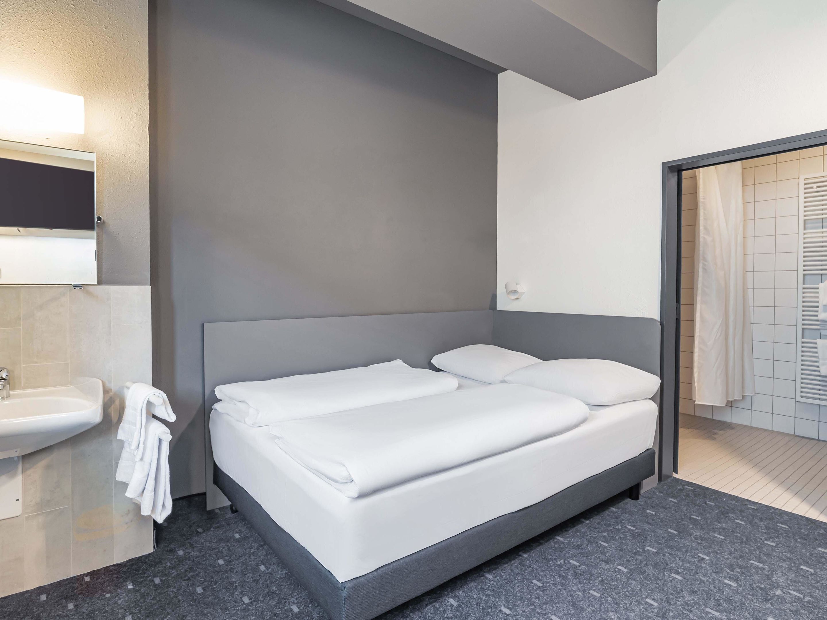Een moderne hotelkamer met een bed, een wastafel en een douche.