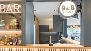 En receptionsdisk med en skylt för B&B Hotels, en bardisk med olika sorters spritflaskor och utsikt över hotellets interiör.