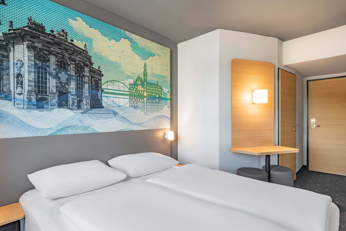 Une chambre d’hôtel avec un lit, une lampe fixée au mur et une porte.