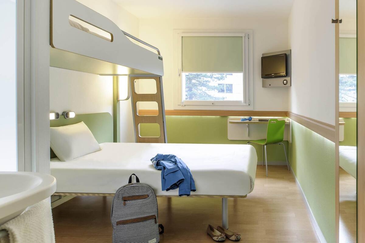 Ein kleines Zimmer mit Etagenbetten, einem Schreibtisch, einem Stuhl, einem Rucksack und einem Paar Schuhe.