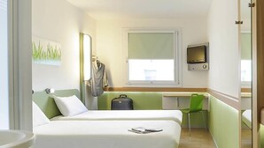 A hotel room with two beds, a desk, a chair, a TV, and a window.