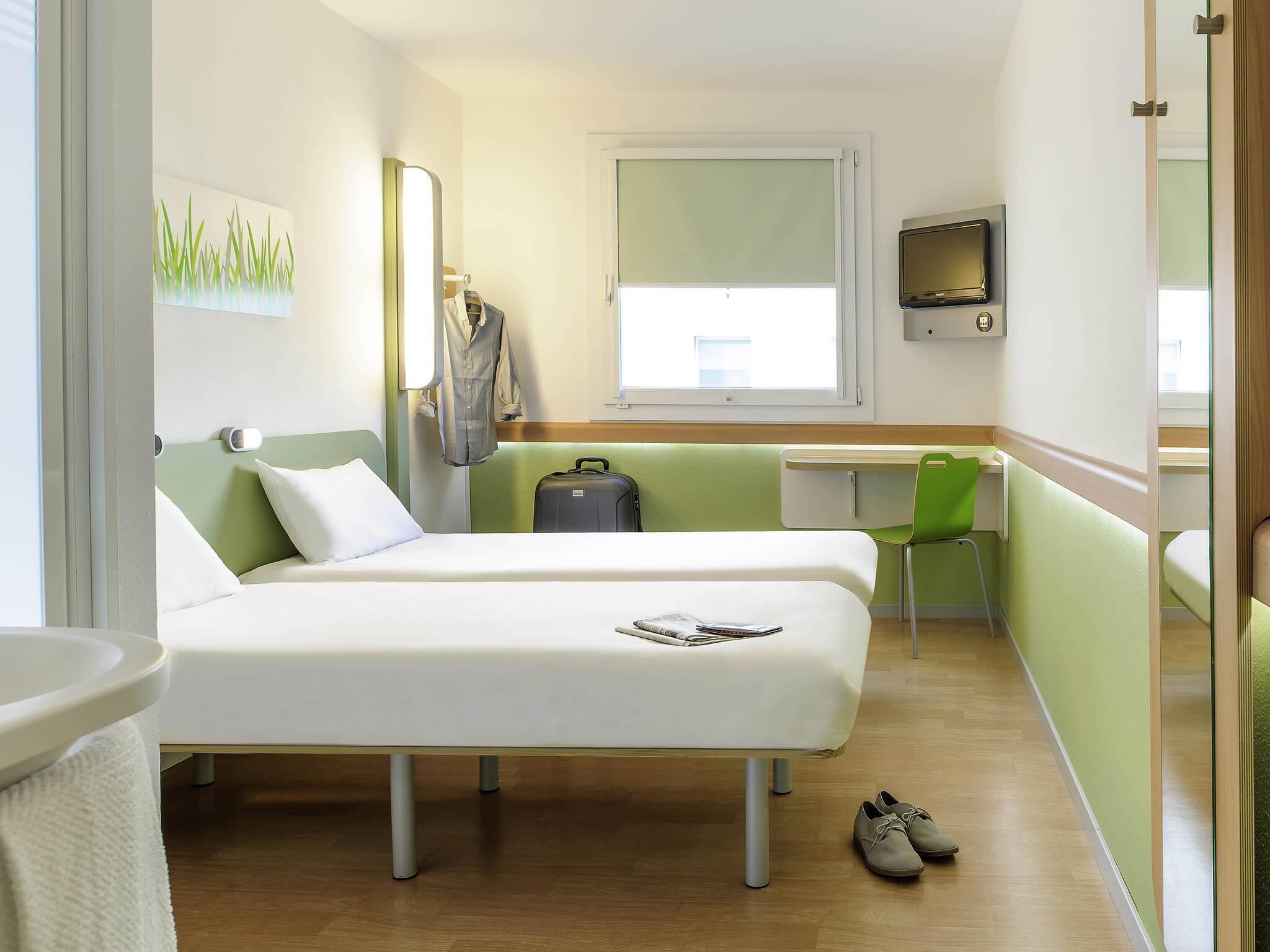 Een hotelkamer met twee bedden, een bureau, een stoel, een televisie en een koffer.