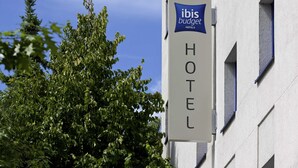 Une enseigne indiquant un hôtel Ibis Budget, avec une vue dégagée sur la façade de l’immeuble et les arbres environnants.