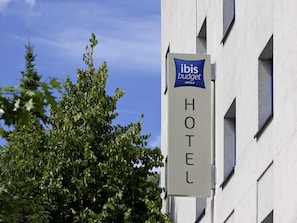Een bord van het ibis Budget Hotel, met een helder zicht op de gevel en de omliggende bomen.