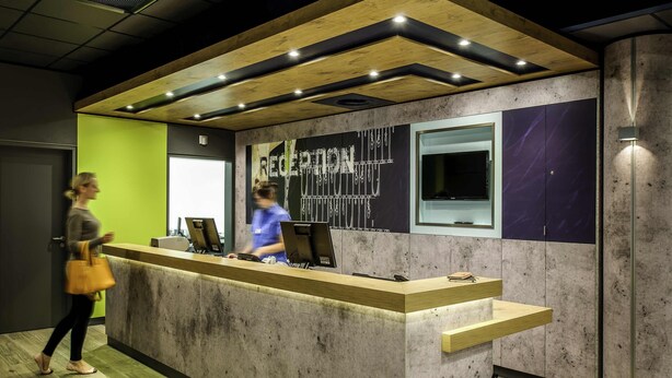 A reception desk with a modern design, featuring a concrete and wood finish, a large window, and a visible counter.