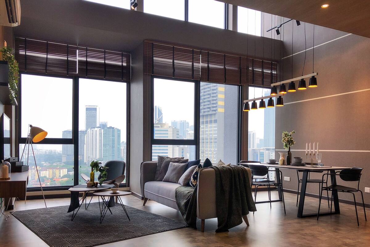 Una sala de estar moderna con un sofá, una mesa de centro y un comedor. Amplias ventanas ofrecen vistas a la ciudad.