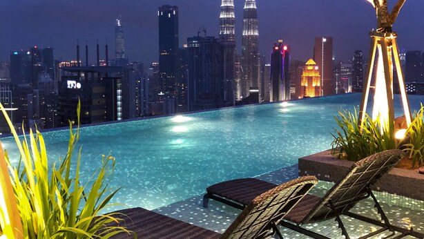 A nighttime pool area with a city skyline in the background, including the Petronas Towers. - Expressionz Professional Suites by Luxurious Lifestyle Living (Kuala Lumpur)
