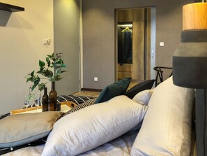 Un dormitorio moderno con una cama, almohadas, una mesita de noche con una planta y un espejo.
