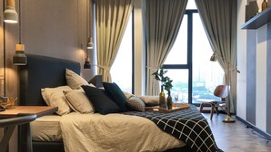 A modern bedroom with a large bed, a desk, and a chair. There are curtains, a window, and a view of the city. - Expressionz Professional Suites by Luxurious Lifestyle Living (Kuala Lumpur)