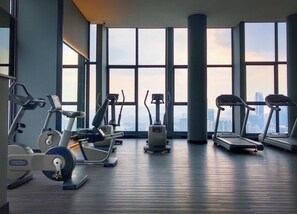 Un gimnasio con máquinas de cardio y un amplio ventanal con vista a la ciudad.