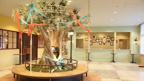 A lobby with a central decorative tree, a reception desk, and a check-in counter.