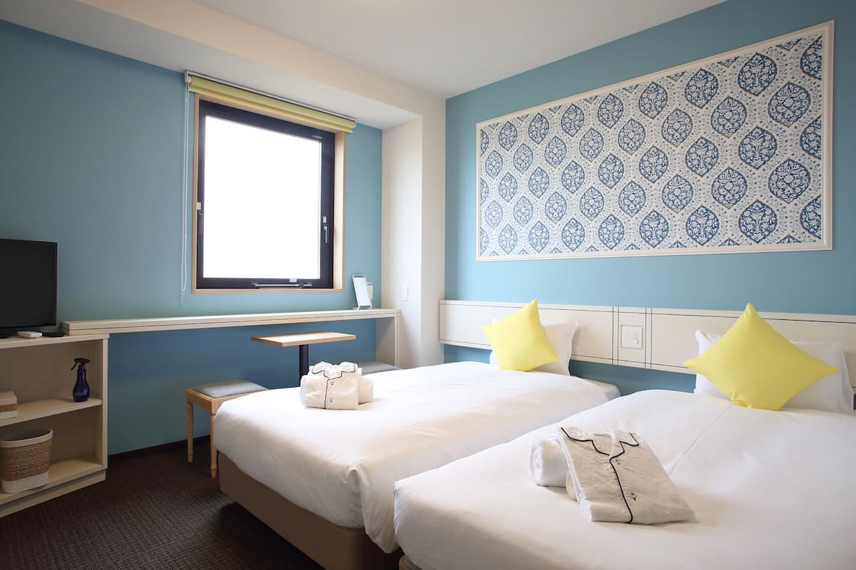 Een hotelkamer met twee bedden, een bureau, een televisie en een raam.