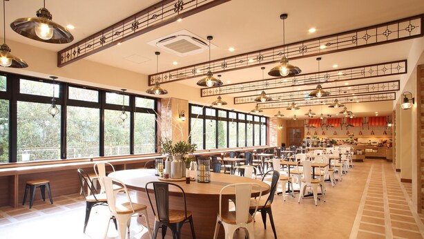 A spacious dining area with multiple tables and chairs, large windows, and hanging pendant lights.
