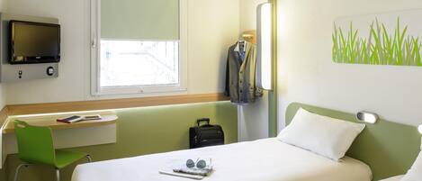 Habitación de hotel con cama, escritorio, silla, televisor y ventana.