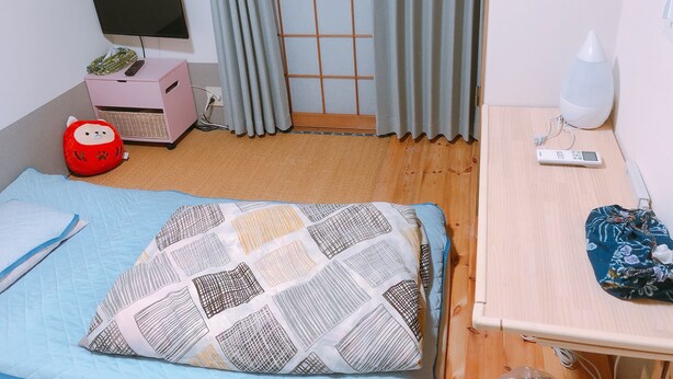 A room with a bed, a desk, a chair, a TV, a lamp, and a window with curtains.