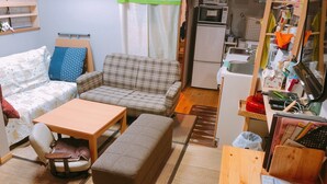 A compact living space with a sofa, a small table, a bench, and a kitchenette area.