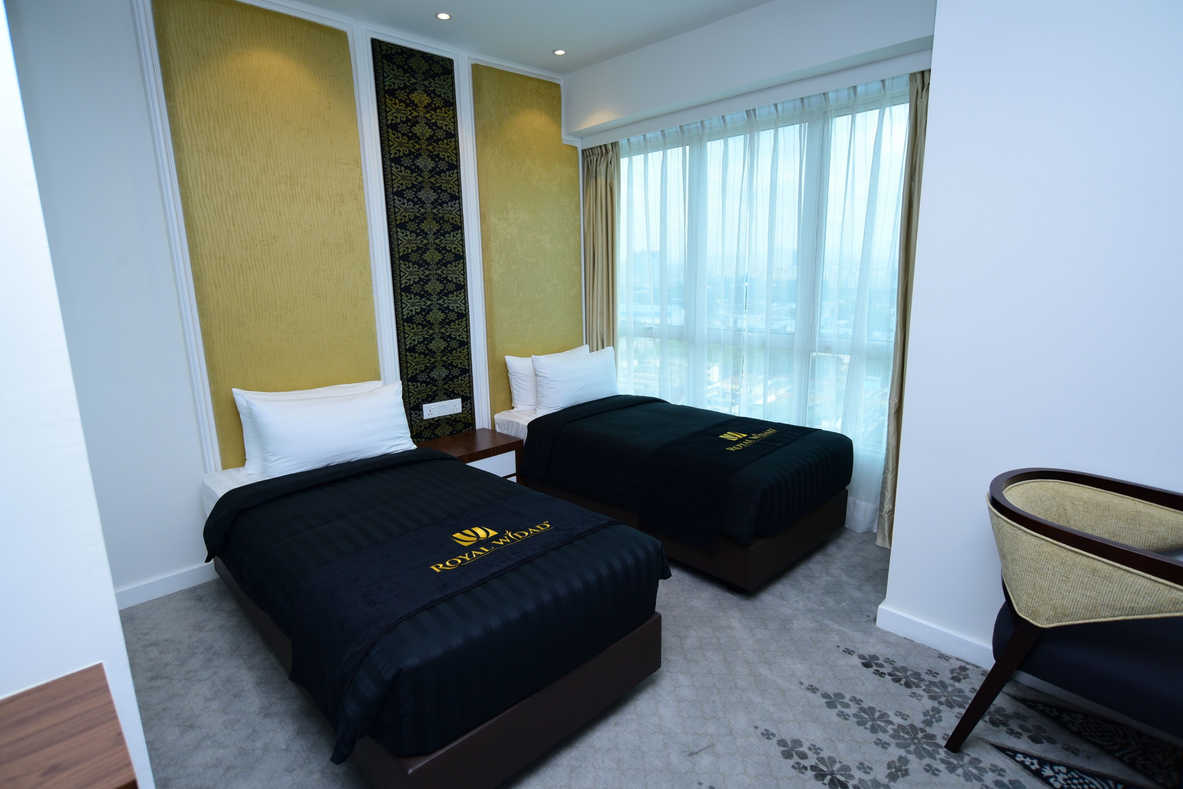 A hotel room with two beds, a chair, and a large window with curtains.