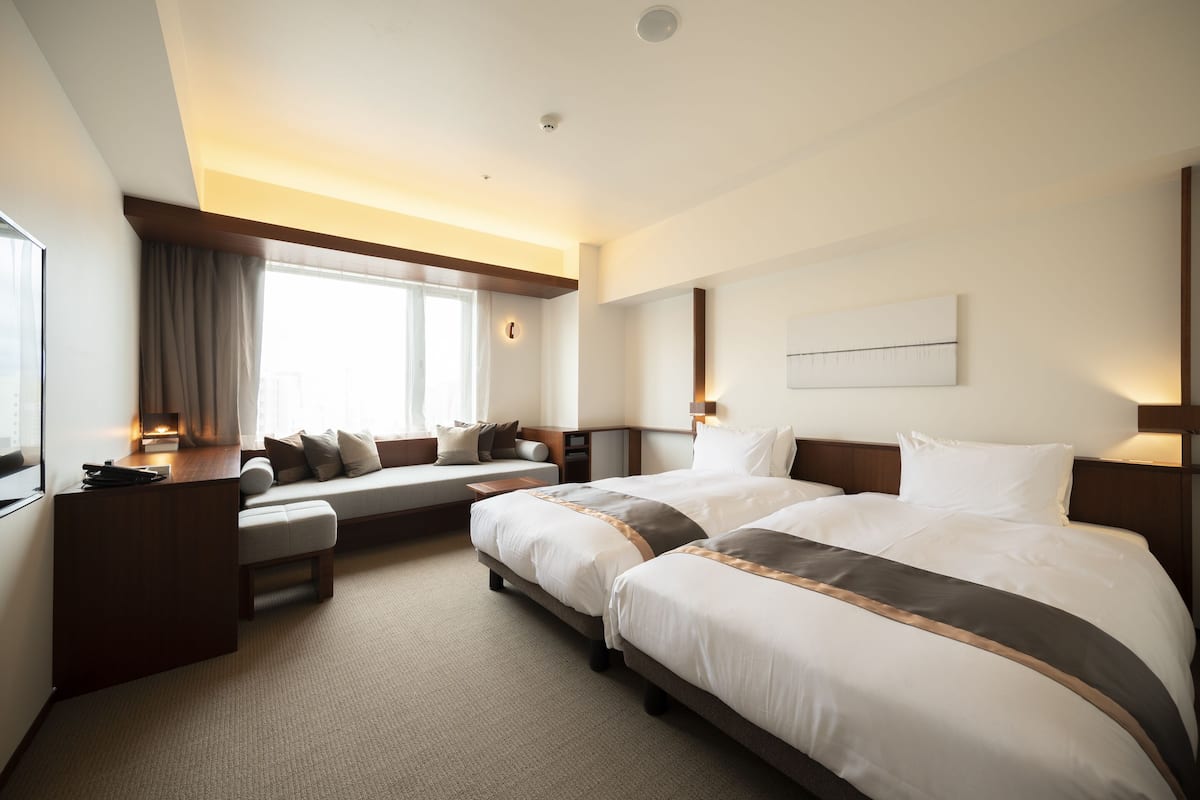 A hotel room with two beds, a sofa, a desk, and a large window.