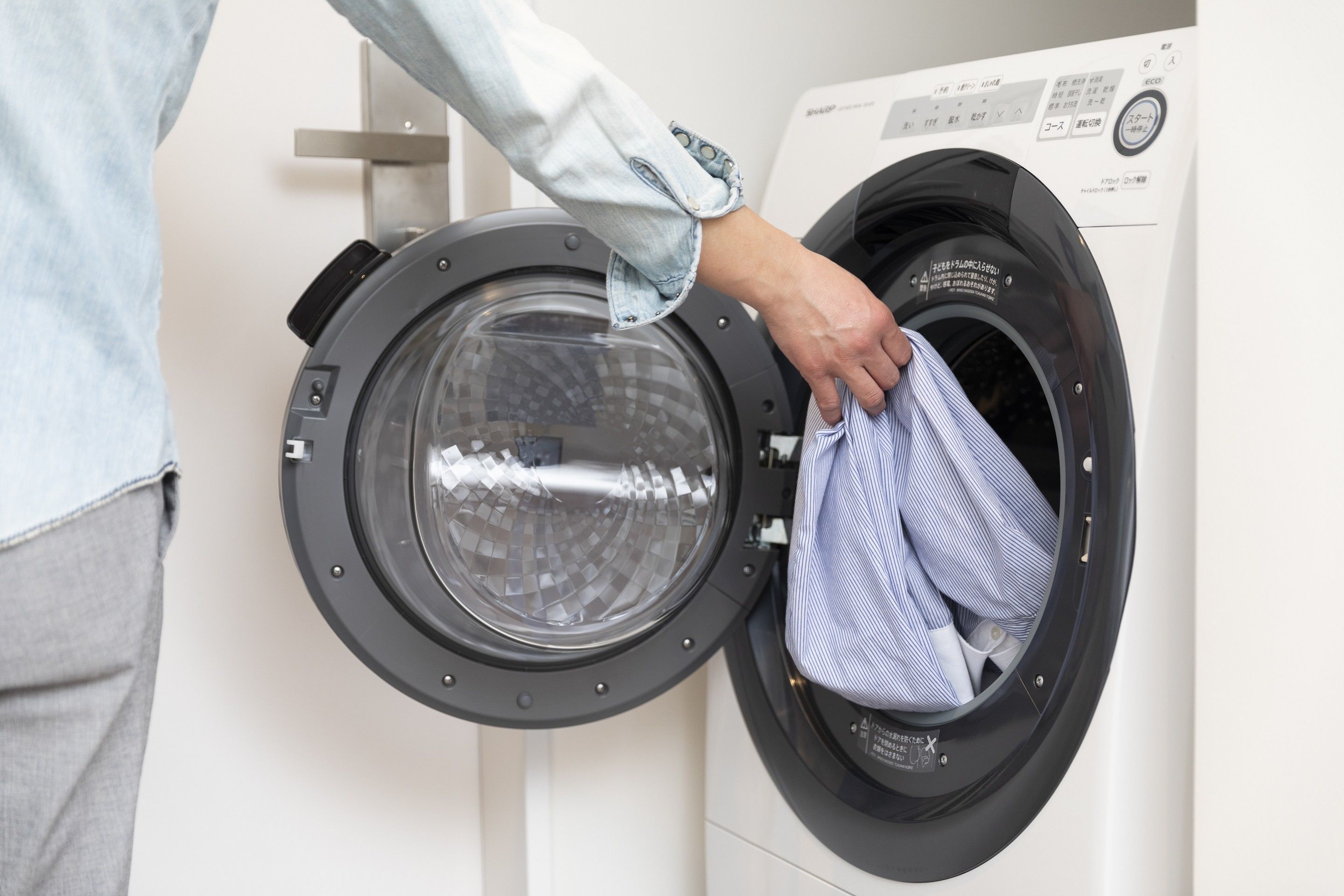 Une personne qui met un vêtement à rayures dans un lave-linge à chargement frontal.