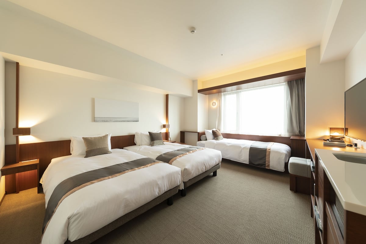 A hotel room with two beds, a desk, a TV, and a window with curtains.