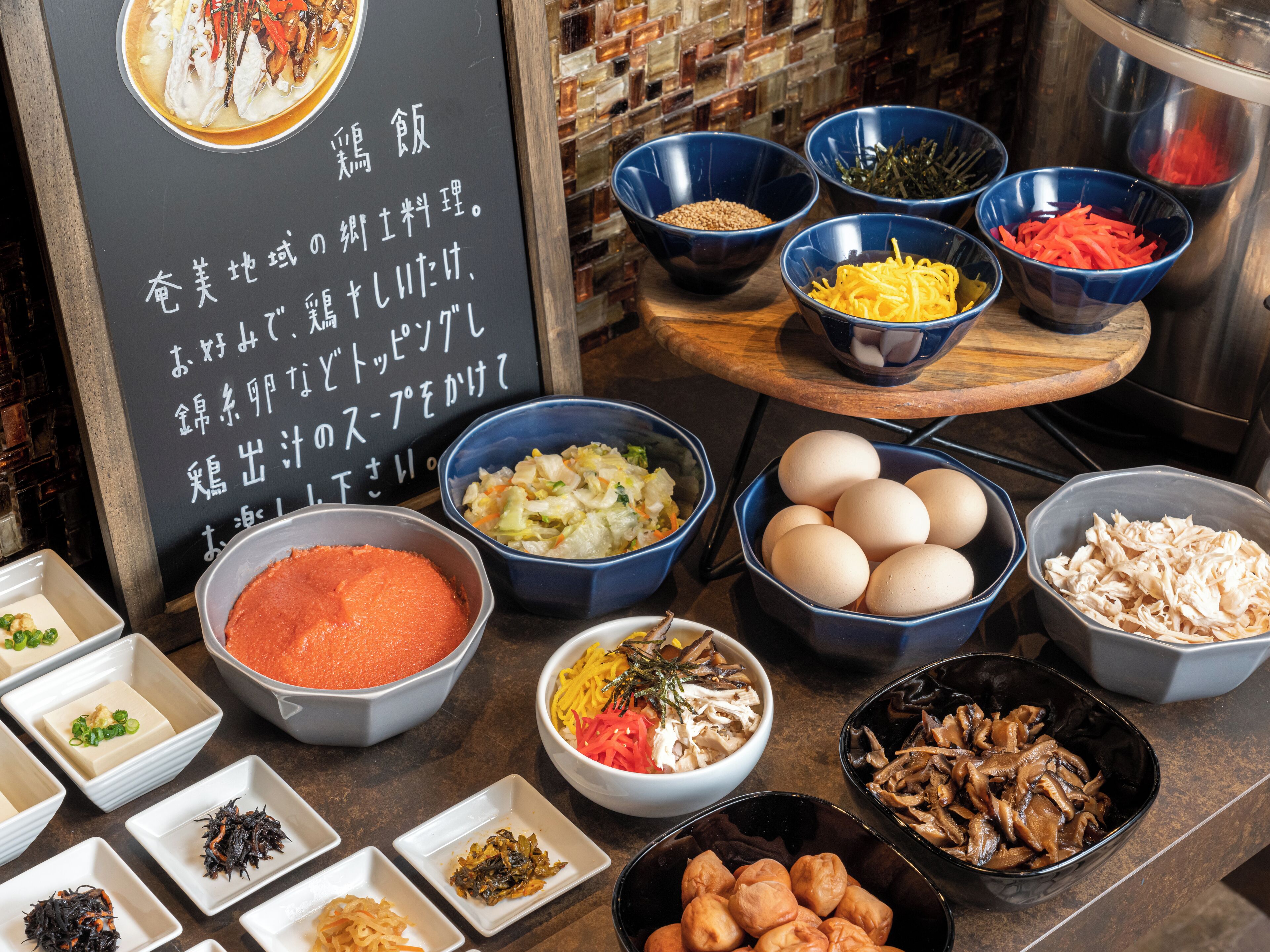A variety of food items and ingredients displayed on a counter, including bowls of vegetables, eggs, and sauces.