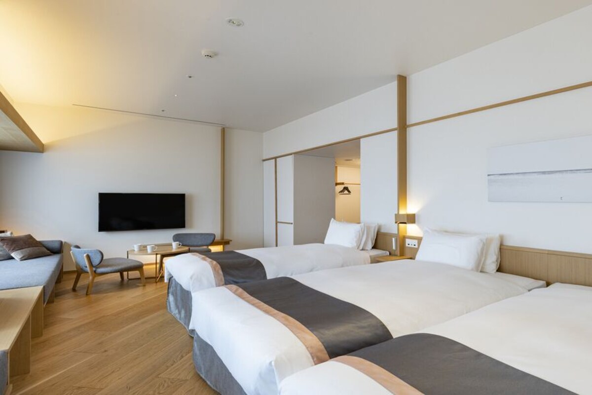 A hotel room with three beds, a TV, a desk, and a chair.