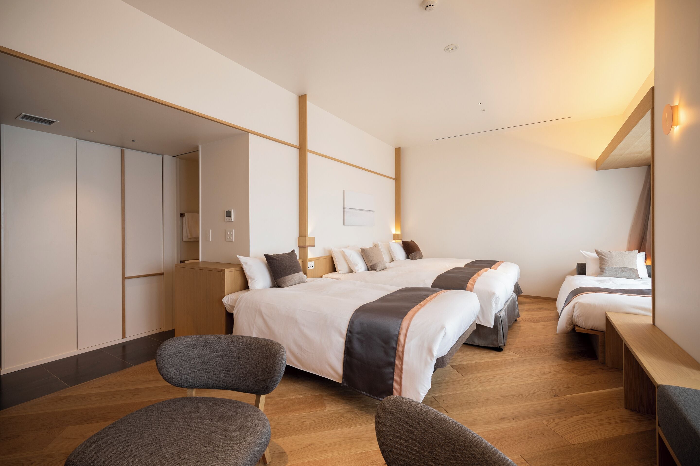 A modern hotel room with a large bed, two smaller beds, a seating area, and a wardrobe.