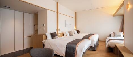 A modern hotel room with a large bed, two smaller beds, a seating area, and a wardrobe.