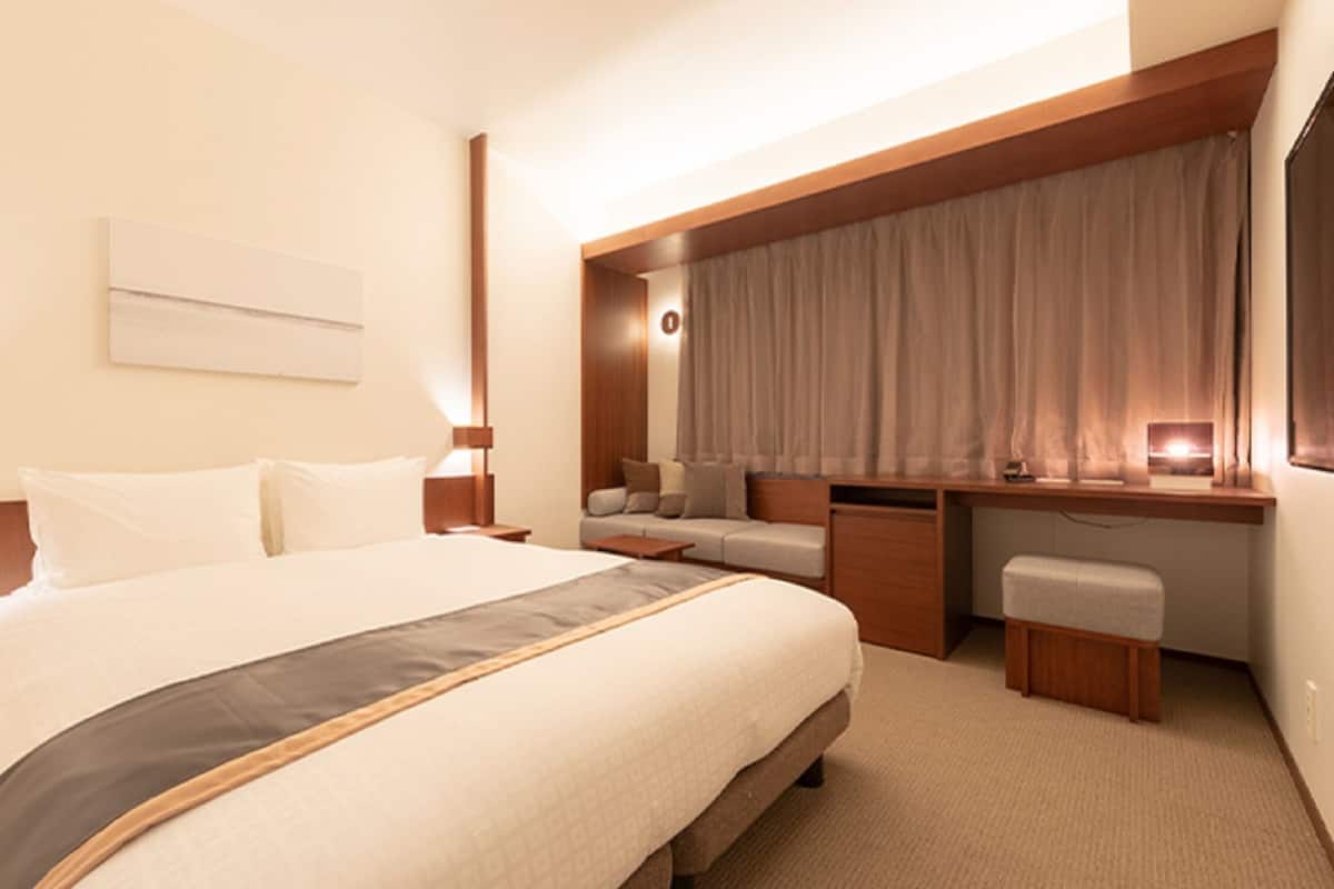 A hotel room with a large bed, a desk, a chair, and a window with curtains.