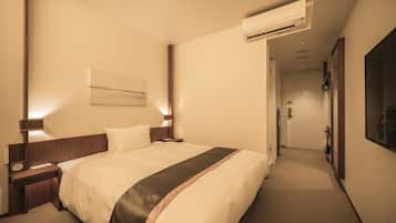 A hotel room with a large bed, bedside tables, an air conditioning unit, and a hallway leading to a door.