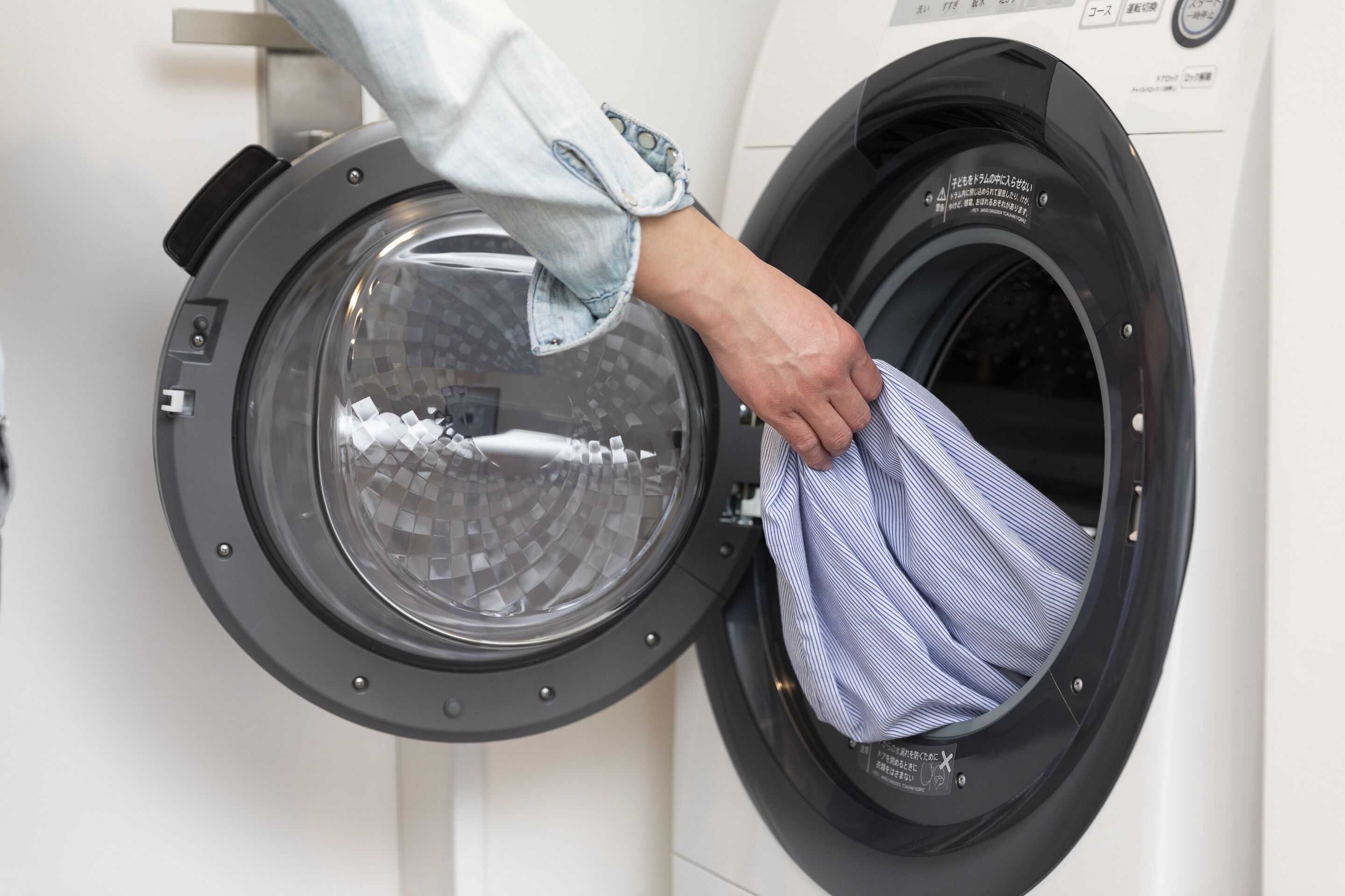 A person placing a striped garment into a front-loading washing machine.