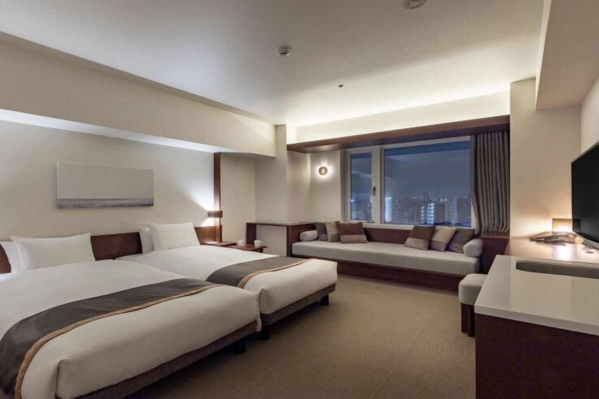 A hotel room with two beds, a sofa, a TV, and a city view.
