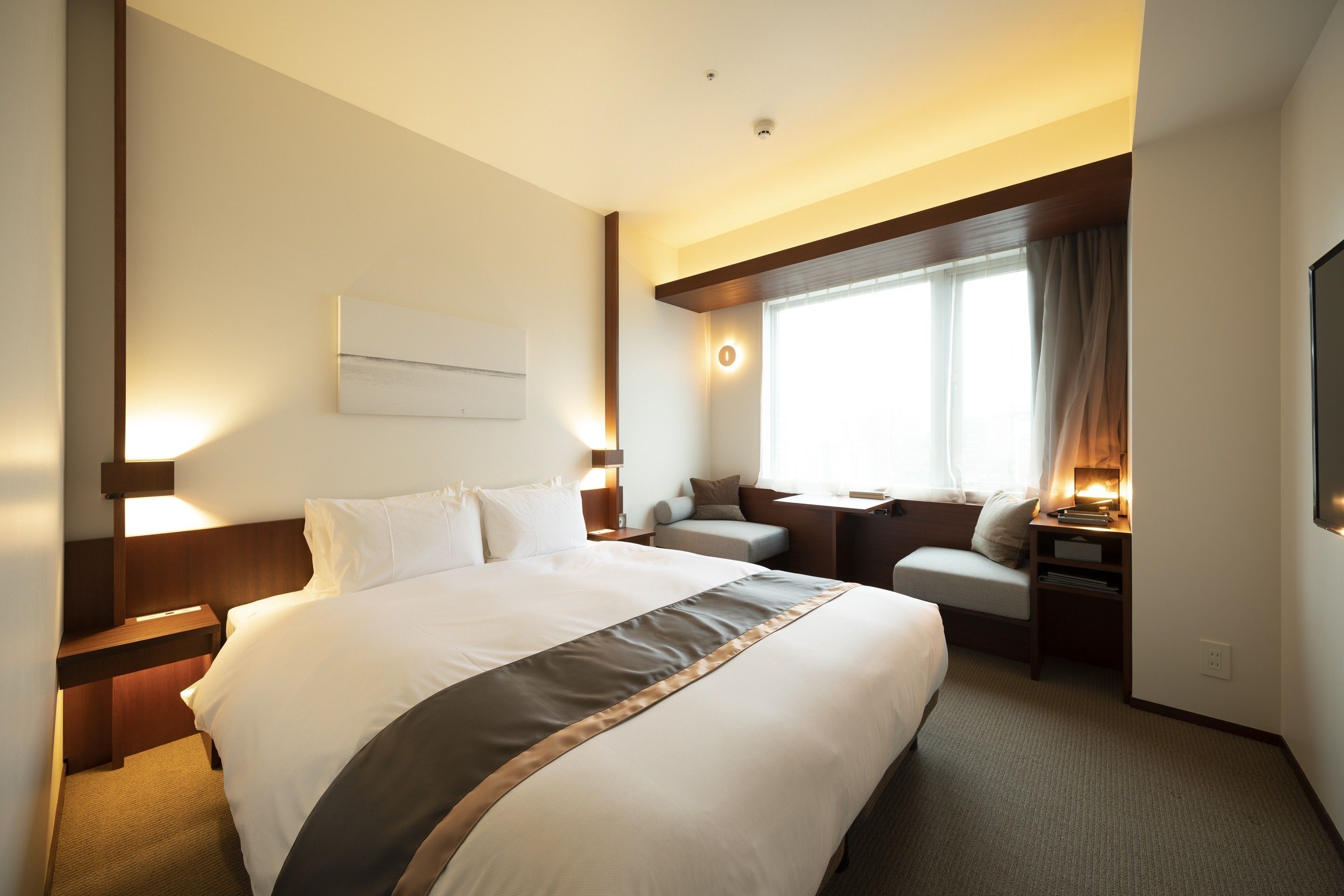 Habitación de hotel con una cama grande, un escritorio, una silla, un televisor y una ventana con cortinas.