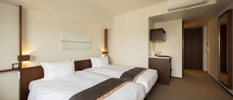 A hotel room with two beds, a desk, a TV, and an air conditioning unit.
