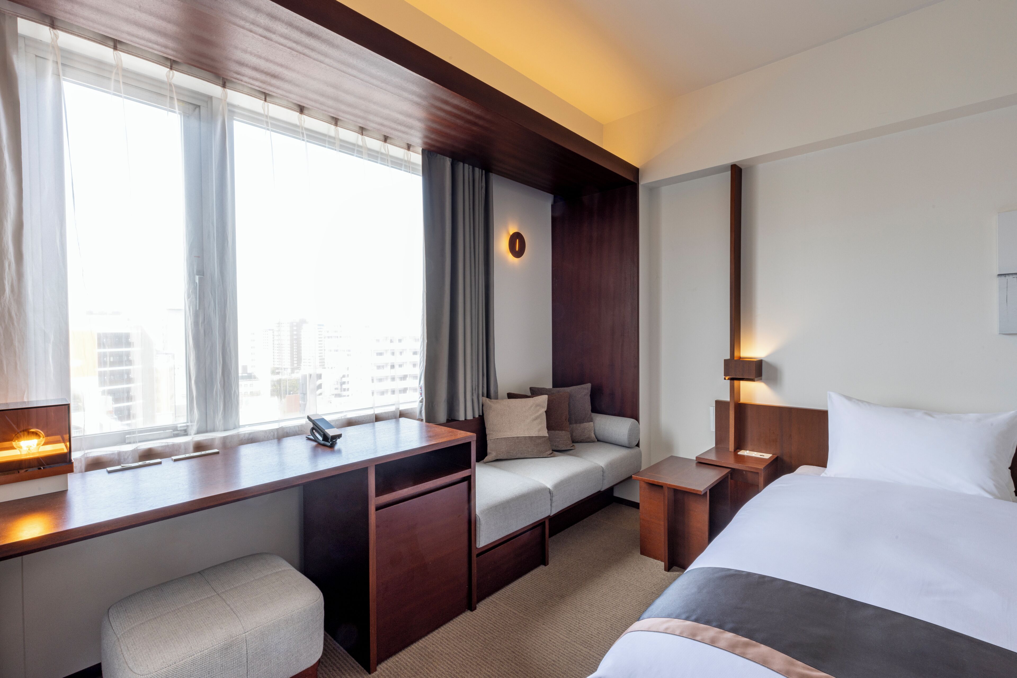 Une chambre d’hôtel comprenant un lit, un bureau, une chaise, un canapé, une table de chevet et une fenêtre avec des rideaux.