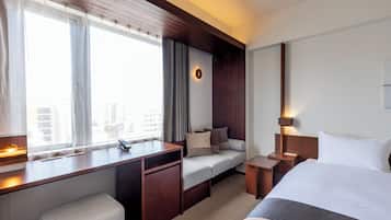 Ein Hotelzimmer mit einem Bett, einem Schreibtisch, einem Sessel, einem Sofa, einem Nachttisch und einem Fenster mit Vorhängen.