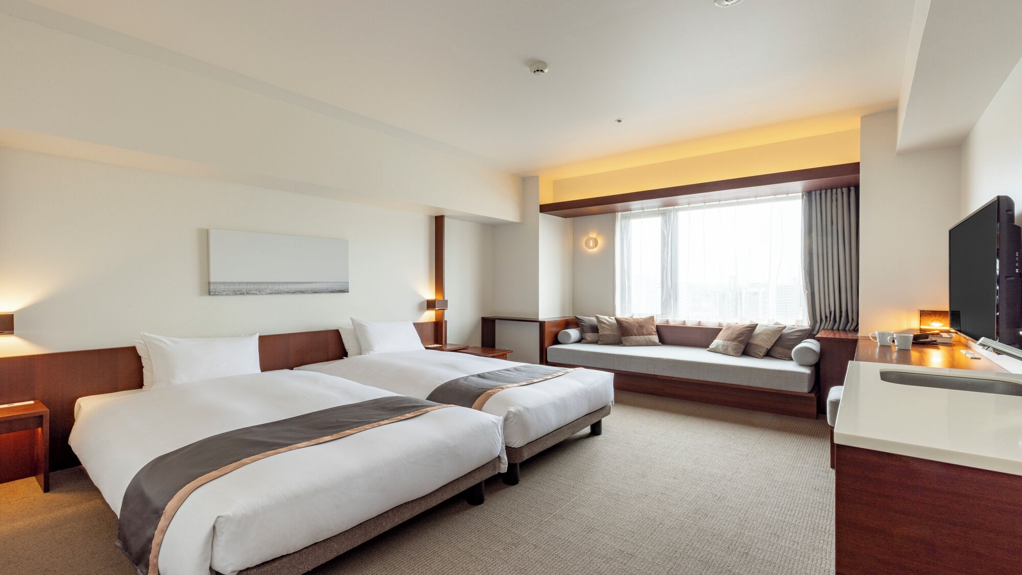 Habitación de hotel con dos camas, un escritorio, un televisor y un ventanal grande con cortinas.