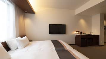 A hotel room with a large bed, a flat-screen TV mounted on the wall, a small kitchenette, and a window with sheer curtains.