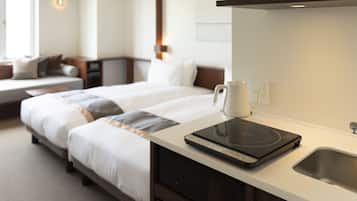 A hotel room with a bed, a coffee maker, a kettle, and a built-in induction cooktop on the counter.
